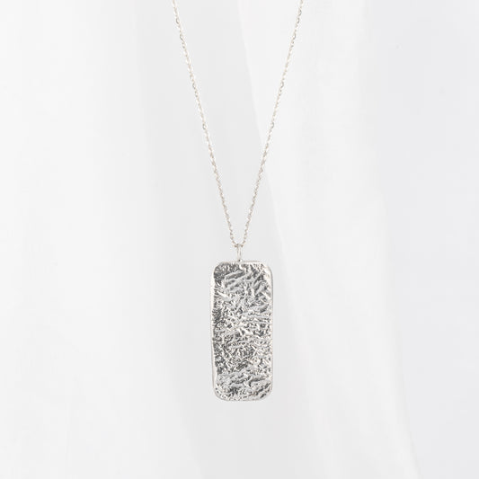 A silver rectangle pendant necklace with textured designs on the pendant, displayed against a light background.