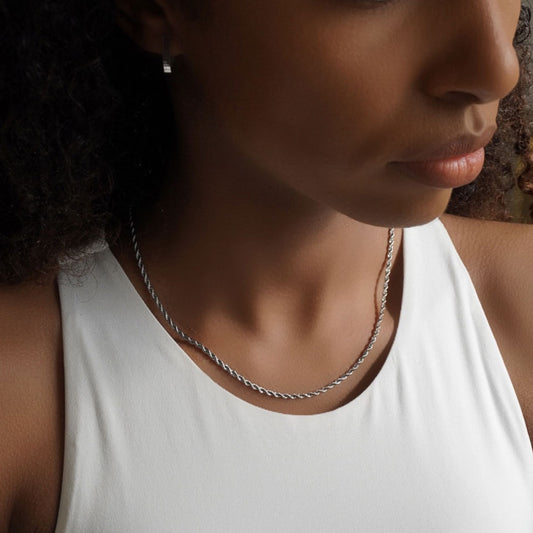 A close-up image of a woman wearing a white tank top, showcasing a silver rope chain necklace.