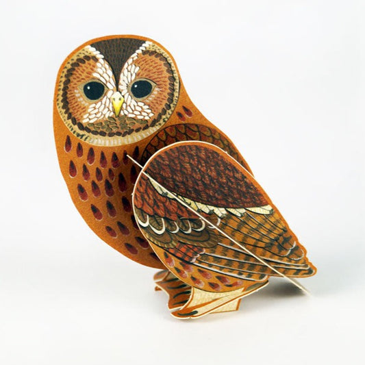 A decorative paper model of an owl, featuring intricate patterns in shades of brown and orange. The owl is depicted in a standing position, showcasing its large eyes and detailed feathers, set against a plain white background.