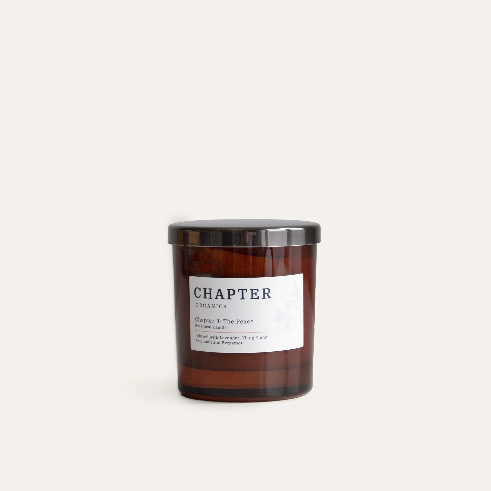 A brown glass candle jar with a black lid, labelled "Chapter Organics" and "Chapter & The Peace." The label features a simple design with text in a clean font, set against a light, neutral background.