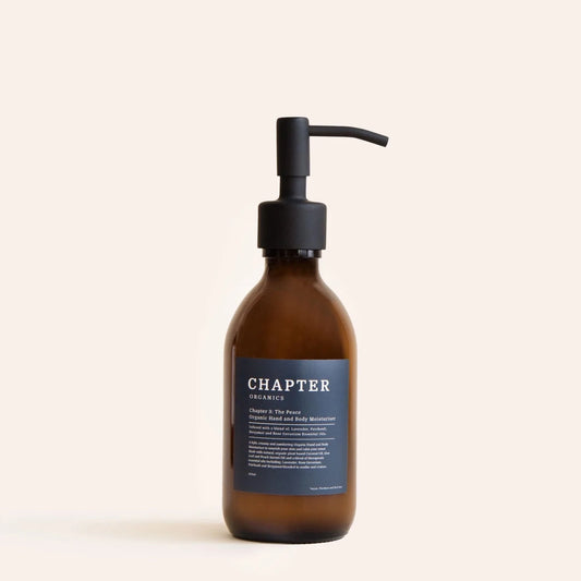 A brown glass bottle with a black pump dispenser, labelled "CHAPTER ORGANICS" in white text. The label features a description of the product and its benefits, set against a light beige background. The overall aesthetic is minimalist and elegant.