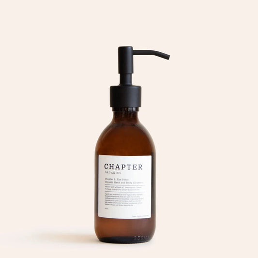 A brown glass pump bottle with a black pump lid. The label features minimalist text, indicating the product name "The Tonic" and a brief description. The background is a soft, neutral colour, enhancing the bottle's elegant design.