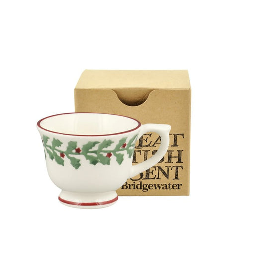Decorative mug with holly design in front of a brown box on a white background