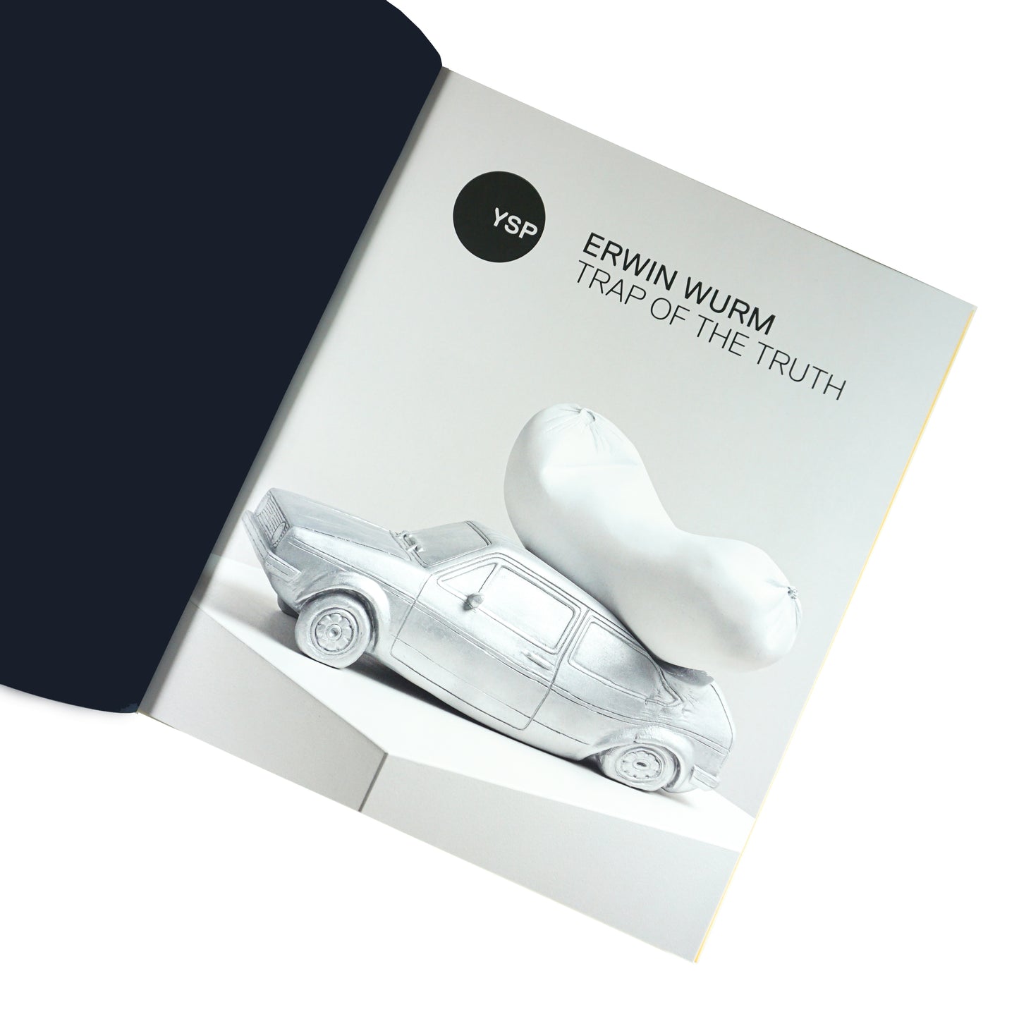 A page from a book featuring a sculpture by Erwin Wurm titled "Trap of the Truth." The artwork depicts a silver car with a large, white, abstract shape resting on top, set against a minimalist background. The title and artist's name are prominently displayed.