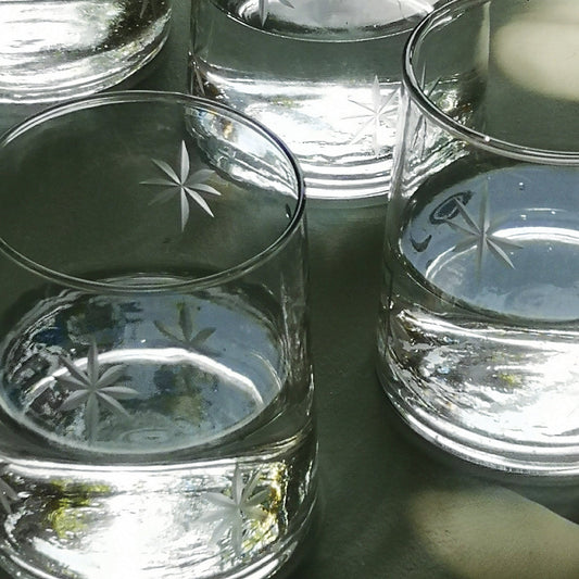 Set of clear glass tumblers with star patterns on a reflective surface