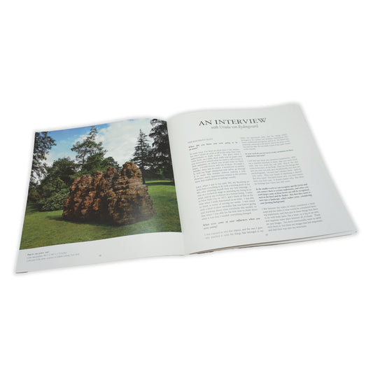 An open book showing  spread with an image of a sculpture in landscape and a page of text opposite.