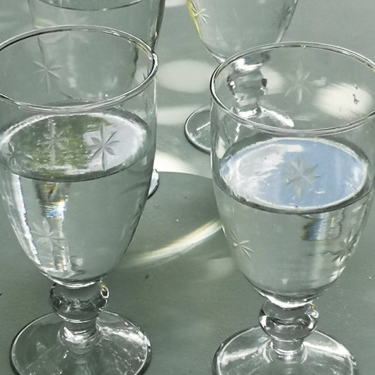 Four clear water glasses with etched star patterns filled with water on a reflective surface.