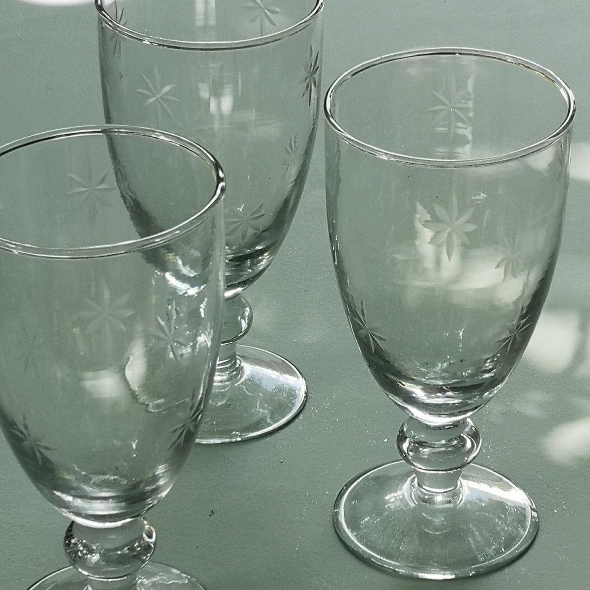 Three clear water glasses with etched star designs on a reflective surface