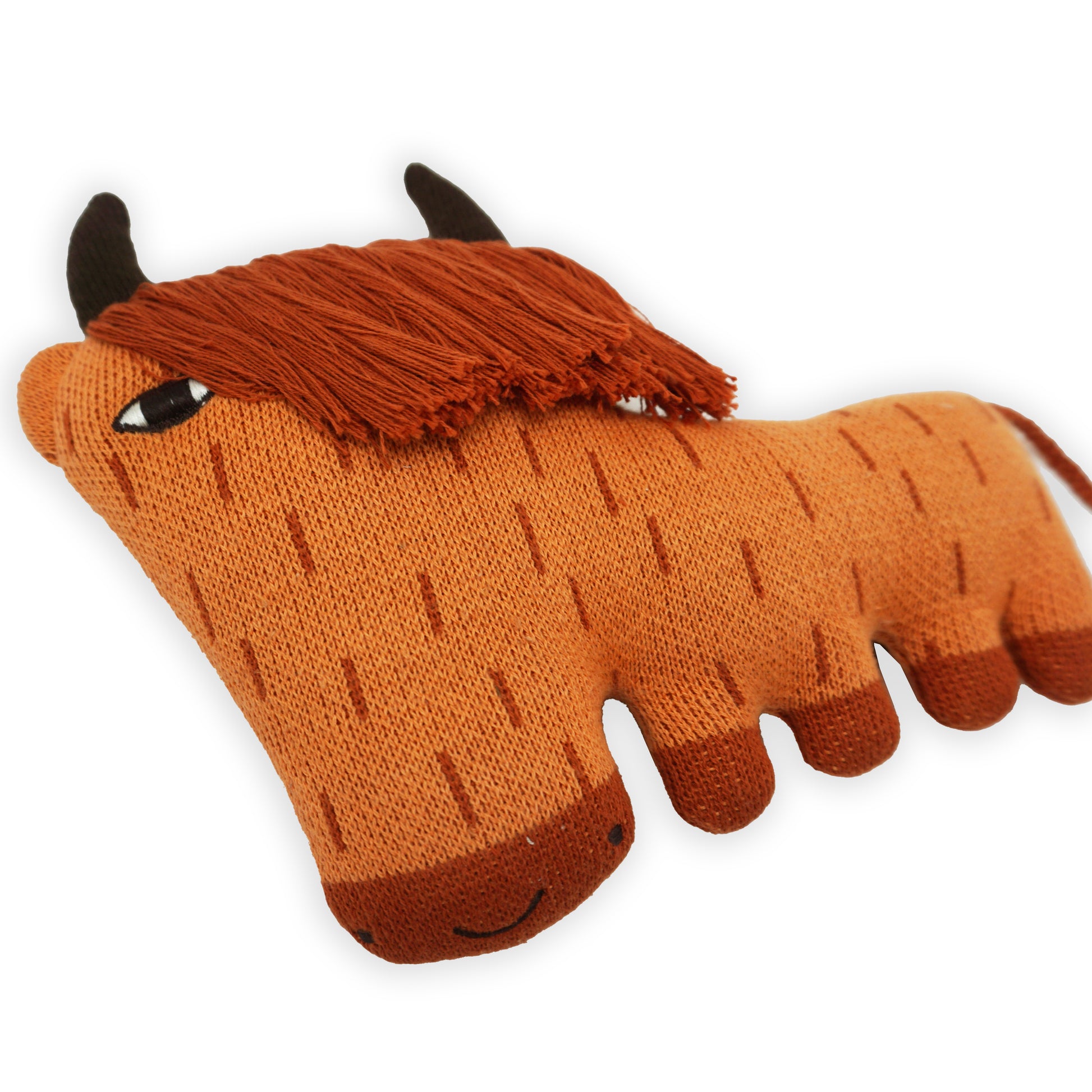 A close up shot of a stylised stuffed orange, brown and red soft toy highland cow with horns and a long fringe and plated tail.
