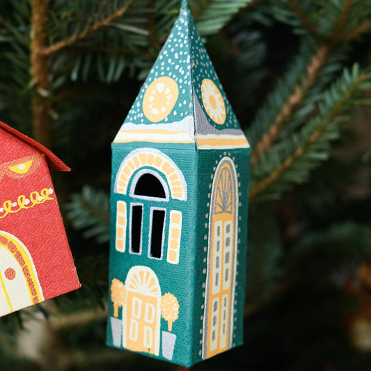 Decorative Christmas tree ornament shaped like a building with a green and gold design, hanging on a tree.