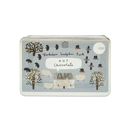 Tin of Yorkshire Sculpture Park hot chocolate. The tin features illustrations of sheep, birds, trees and a house. The tin is placed on a plain white background.