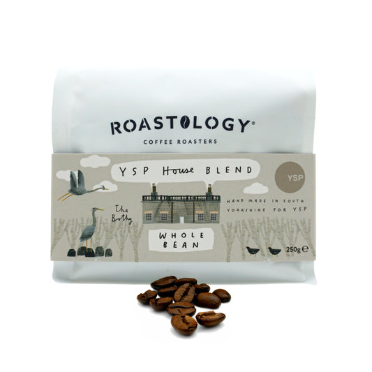 A white packet featuring a pink label with illustrations of British birds and trees, with a pile of coffee beans in front.