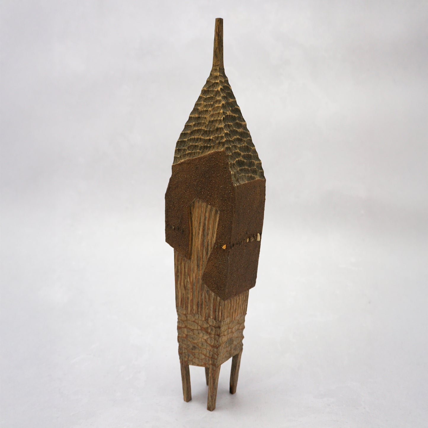 A pointy wooden house with a hand carved roof and body. The house has four legs and small wooden windows on the front.