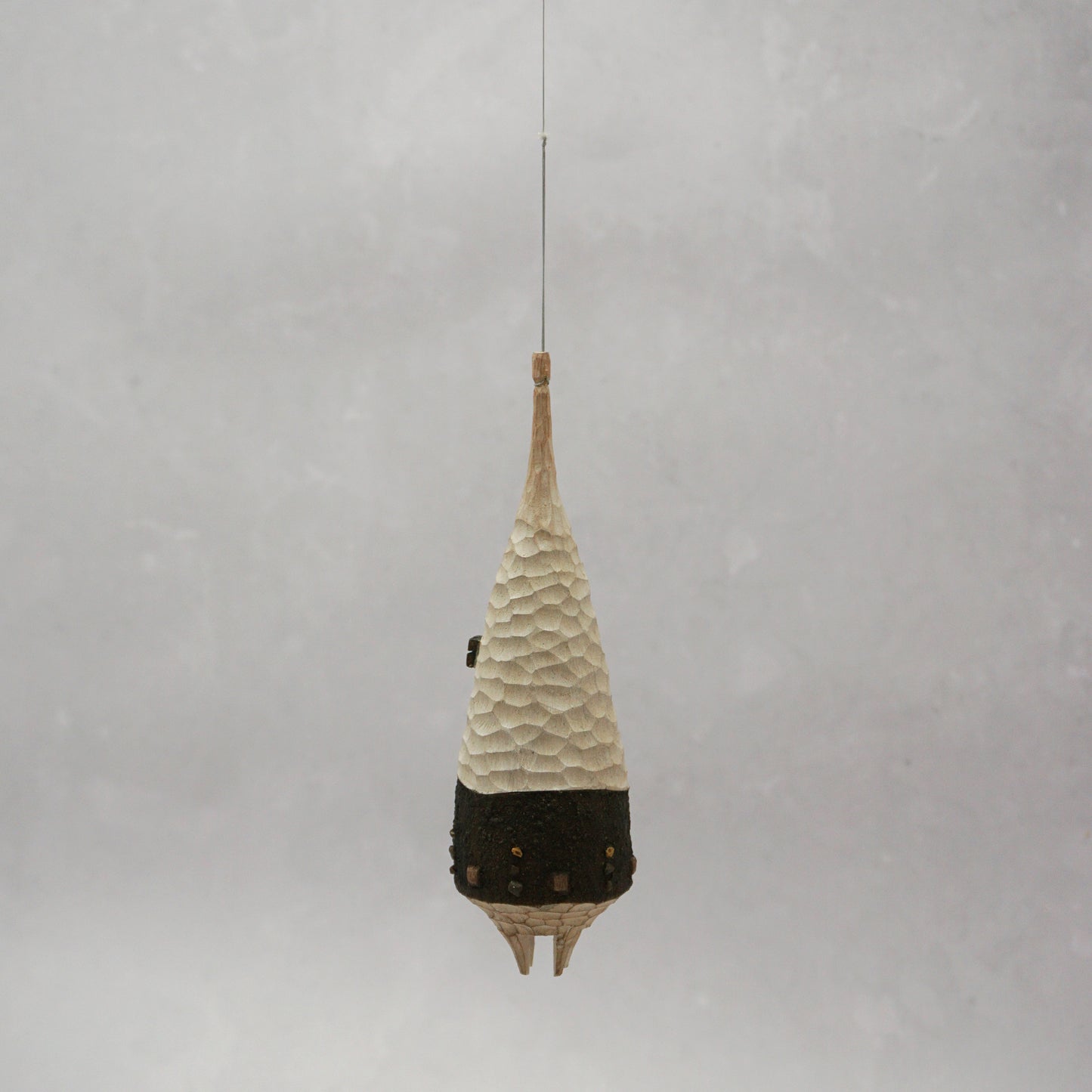 Decorative hanging wooden house with textured design on a plain background. The house has four legs and wooden windows, and is shaped almost like a beehive.