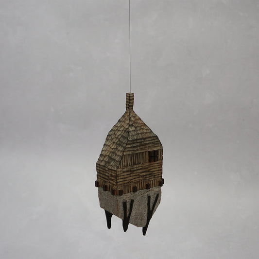 Decorative hand carved wooden house shaped like a small tower on a plain background. The house has legs, windows and a thin chimney which thread is coming out of t hang the house.