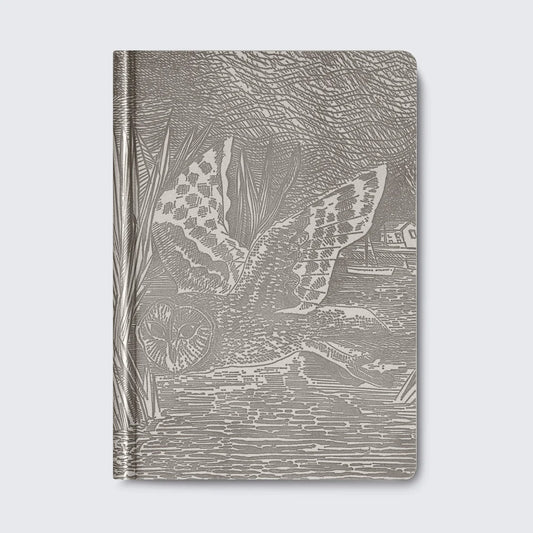A grey notebook featuring an intricate illustration of an owl in flight, surrounded by reeds and a serene water scene. The design is detailed and textured, creating a striking visual effect on the cover.