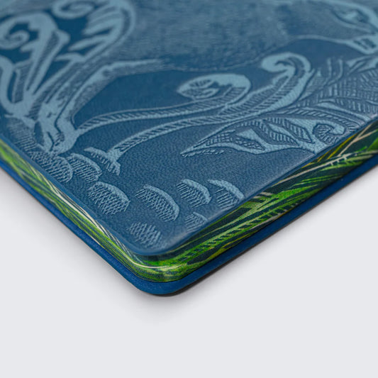 A close-up of a textured blue notebook cover featuring intricate embossed patterns. The edges are highlighted in vibrant green, adding a striking contrast to the overall design. The image captures the detail and craftsmanship of the notebook.