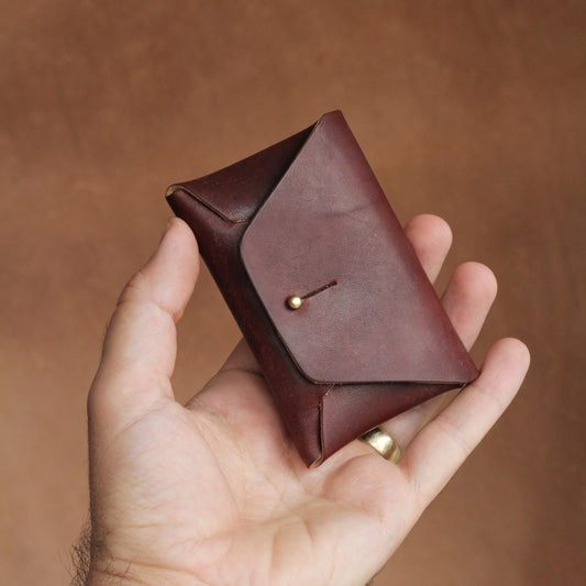 A simple and elegant brown leather card wallet held in a person's hand against a brown background.