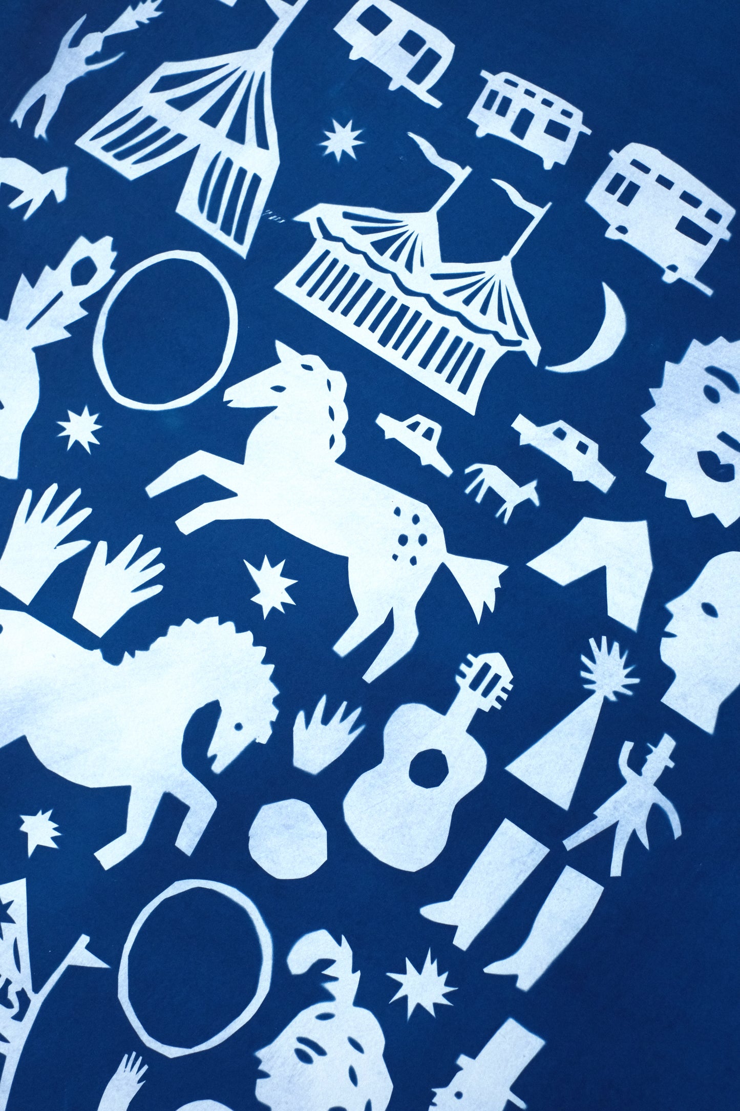 A blue background features a collage of white silhouettes, including a circus tent, horses, a guitar, various faces, and whimsical figures. The design is playful and artistic, showcasing a variety of shapes and motifs in a folk art style.