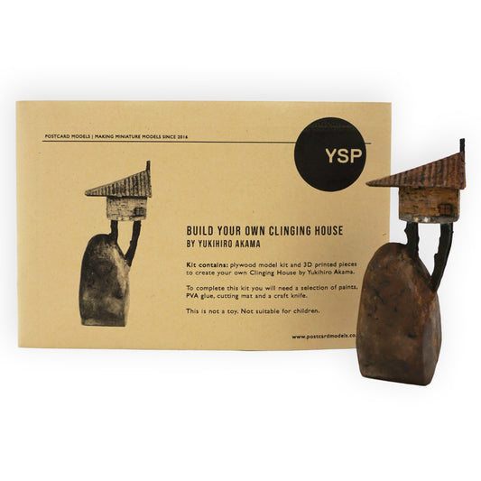 Packaging of the Clinging House postcard model kit with images showing the crafted wooden house and the included 3D printed boulder component.