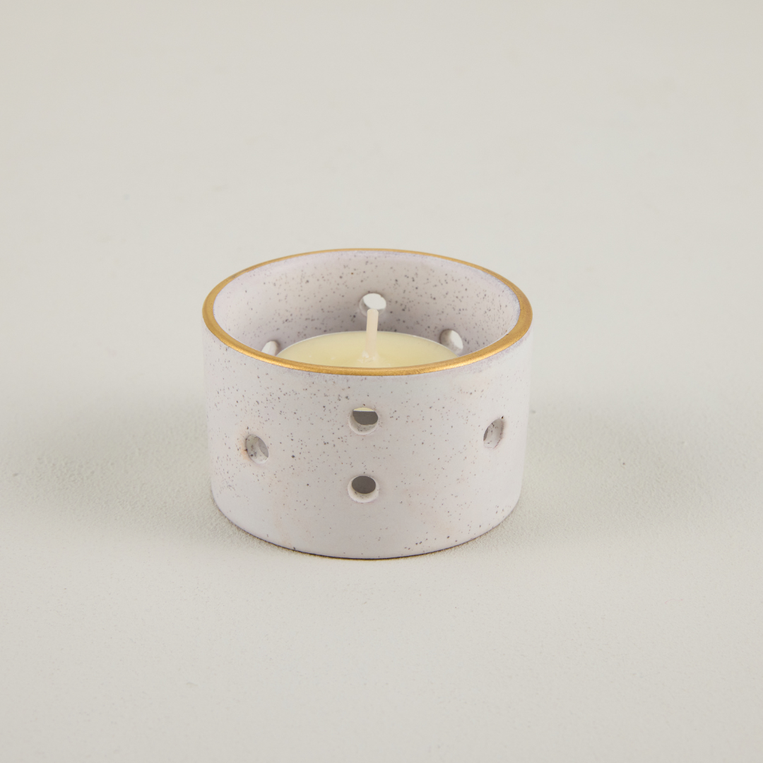 Speckled ceramic candle holder with a lit candle on a light gray background