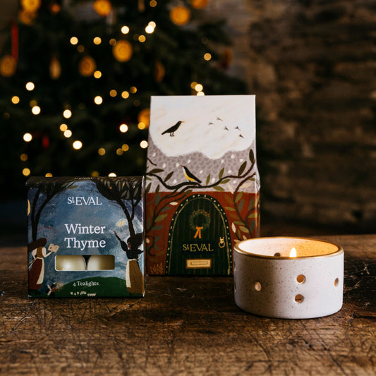 St Eval paper cottage packaging featuring a snowy roof and brown door, next to a small box of tealights and a ceramic candle holder.