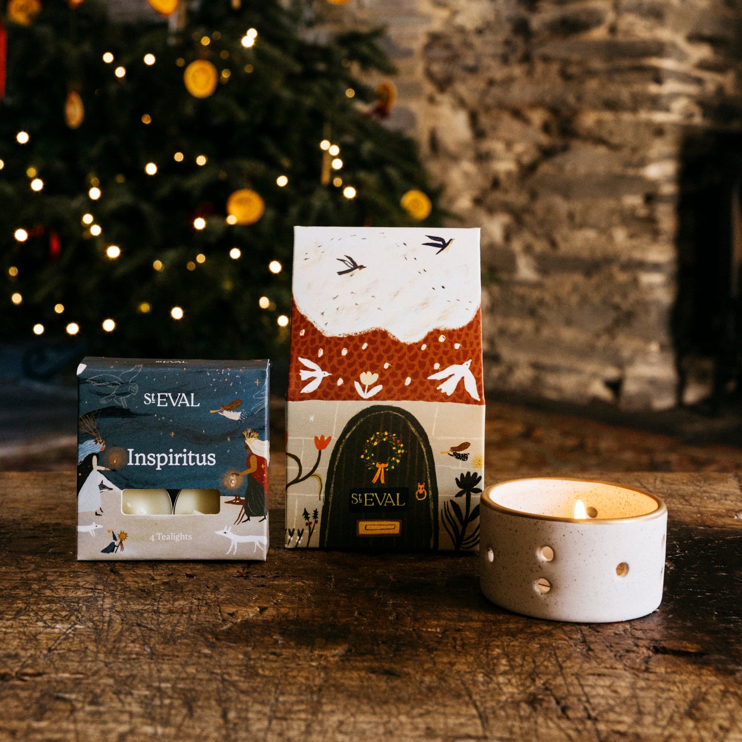 St Eval paper cottage packaging featuring a snowy roof and brown door, next to a small box of tealights and a ceramic candle holder.