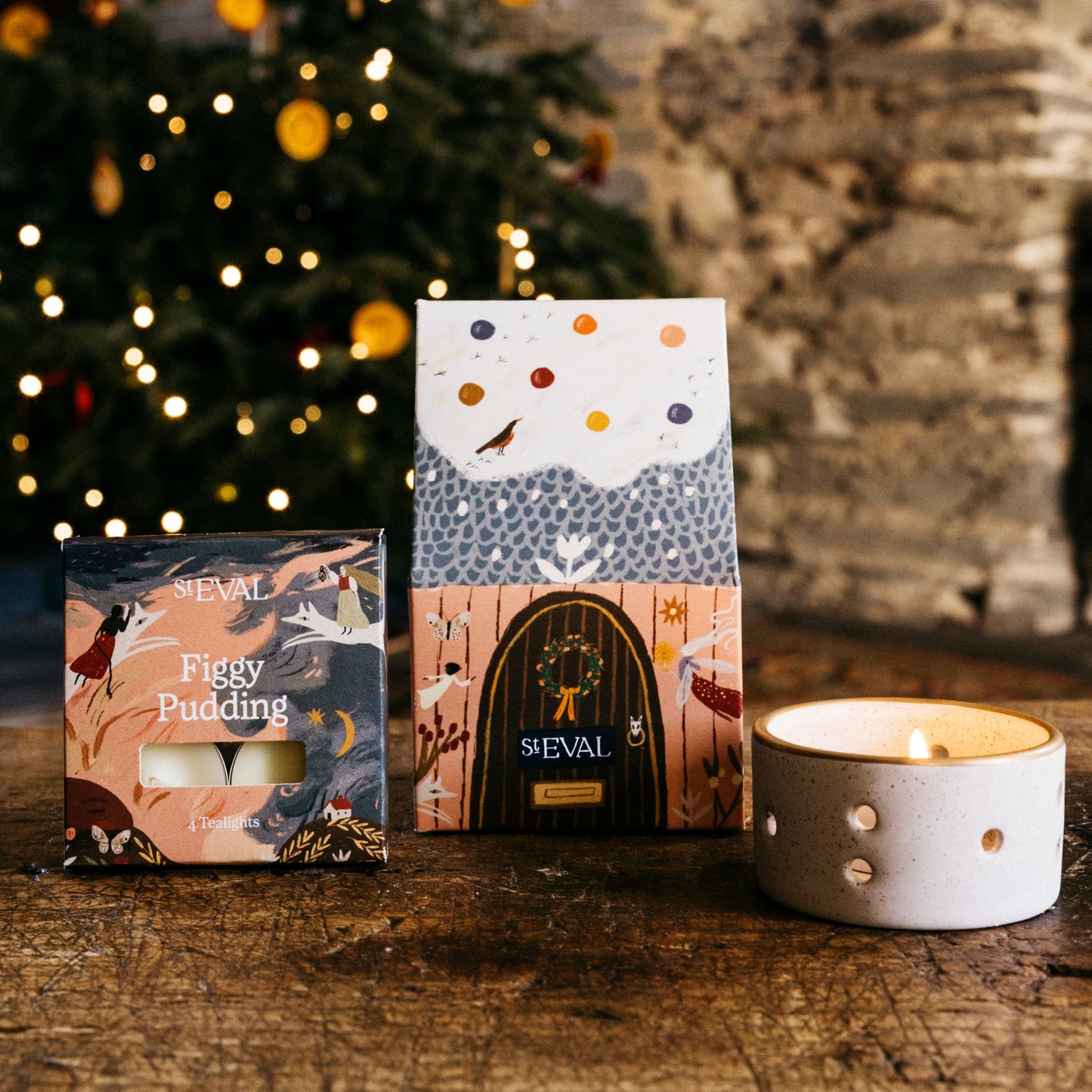St Eval paper cottage packaging featuring a snowy roof and brown door, next to a small box of tealights and a ceramic candle holder.