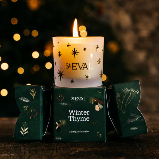 Candle in a decorative box labeled 'SIEVAL Winter Thyme' with a blurred festive background.
