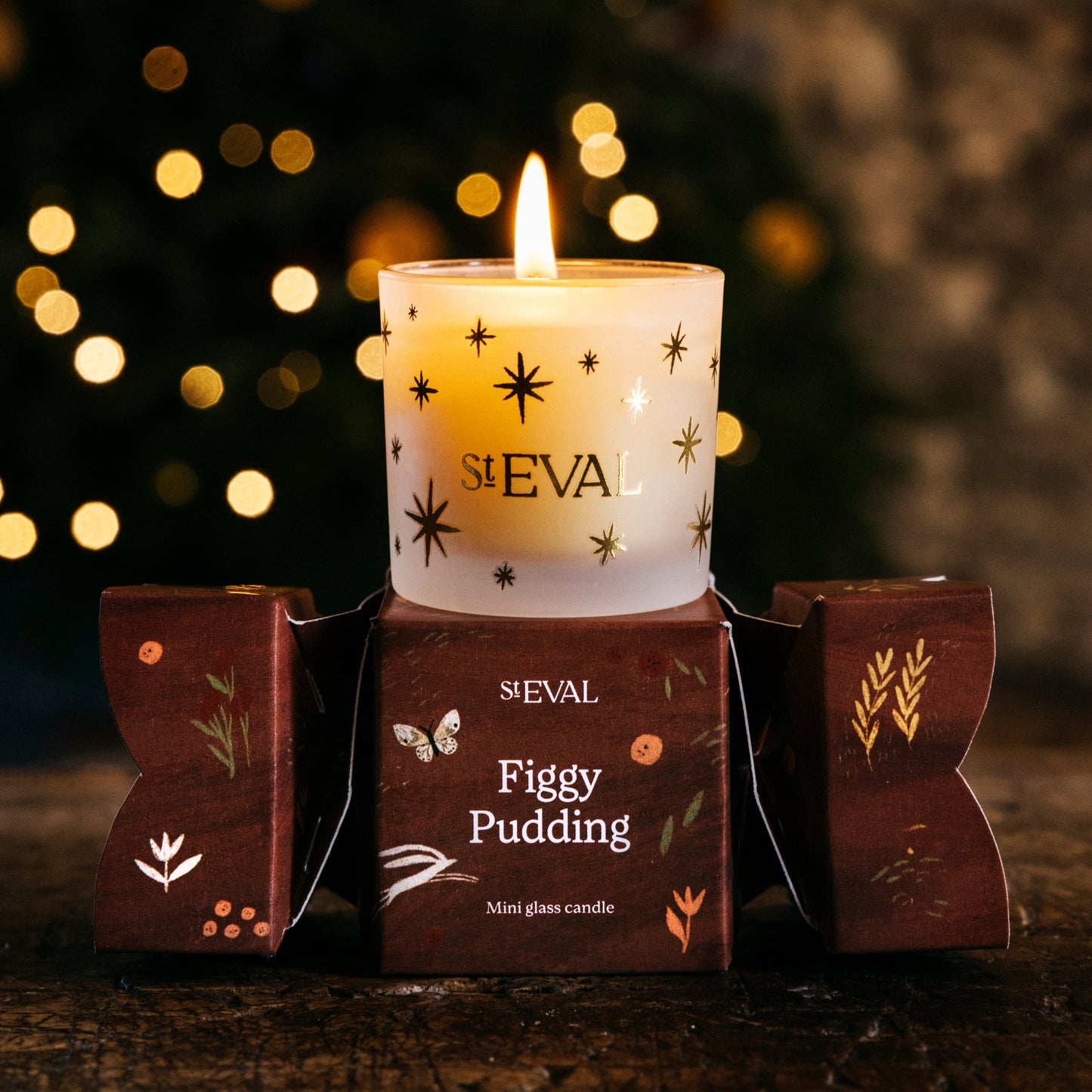 Candle in a decorative holder with 'ST EVAL' branding against a blurred festive background