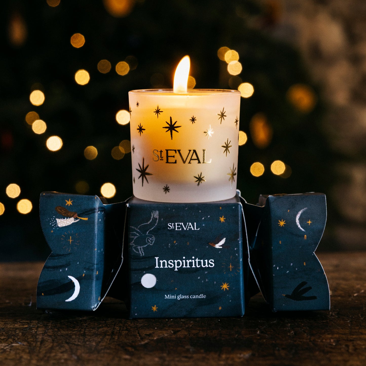 Candle with 'ST EVAL' branding in front of a blurred Christmas tree with lights.