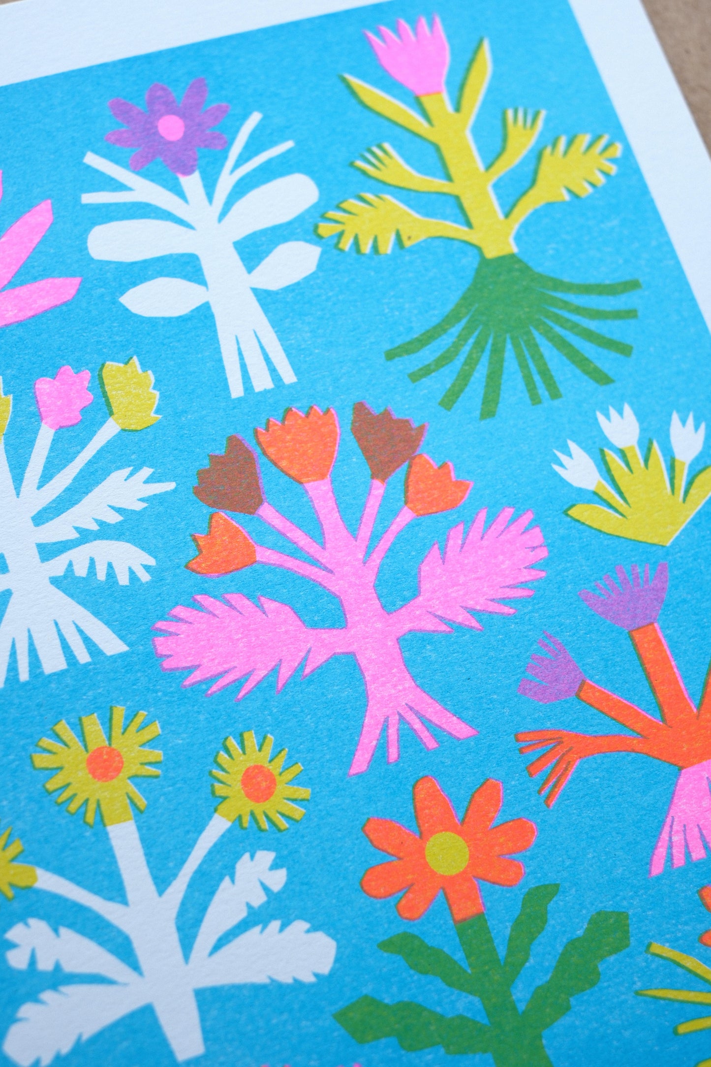 A vibrant illustration featuring a variety of stylised flowers in bold colours, including pink, yellow, and white, set against a bright blue background. The design showcases different floral shapes arranged in a grid pattern.
