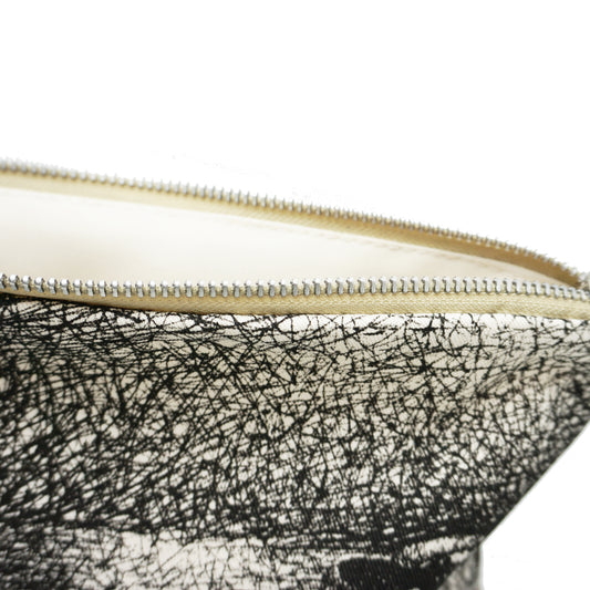 A close-up of a zippered pouch featuring a textured black and white design. The zipper is partially open, revealing a light-coloured interior. The fabric has a sketch-like appearance, adding an artistic touch to the accessory.
