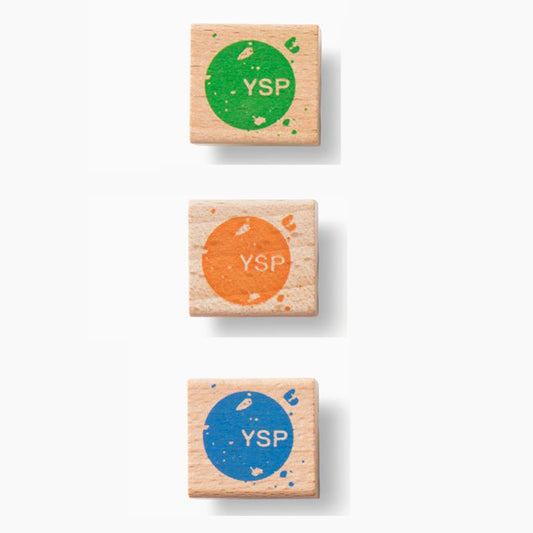 Three wooden pencil sharpeners stacked vertically, each featuring a circular design with the letters "YSP" in the centre. The top sharpener is green, the middle sharpener is orange, and the bottom sharpener is blue.