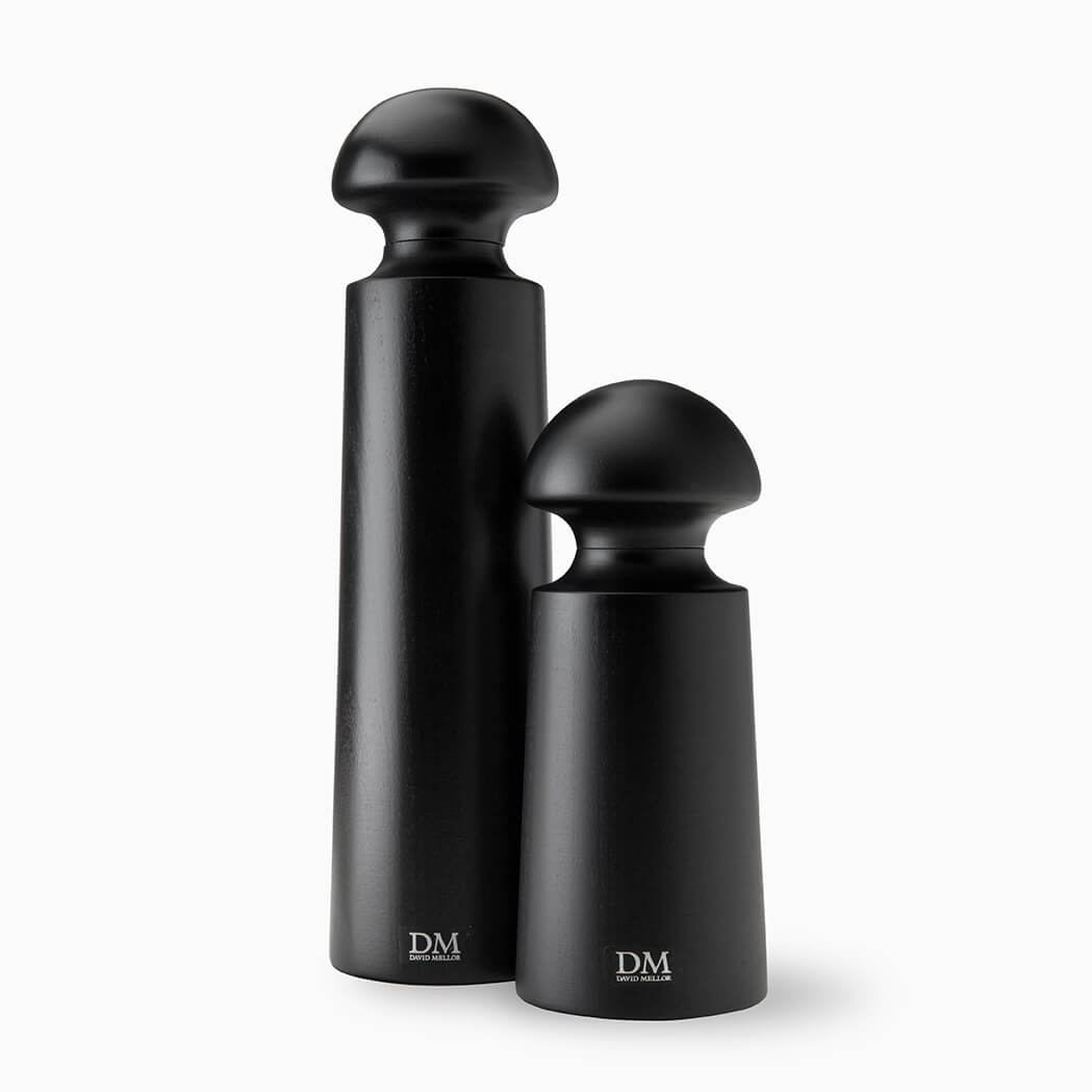 Two sleek, black wooden pepper and salt mills stand side by side. The taller mill has a smooth, elongated body with a rounded top, while the smaller one features a similar design but is more compact. Both have a minimalist aesthetic.