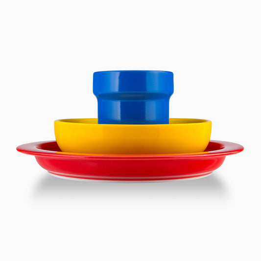 A stack of three brightly coloured plates: a large red plate at the bottom, a medium yellow plate in the middle, and a small blue cup on top. The vibrant colours create a playful and cheerful appearance.
