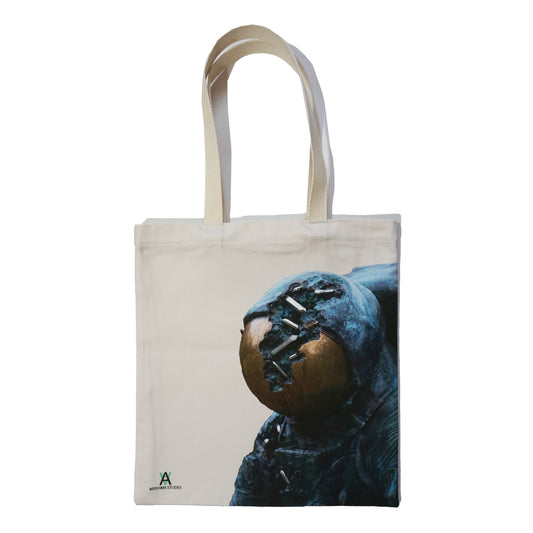 A canvas tote bag featuring a close-up image of a distressed astronaut helmet, with a cracked gold visor. The bag has sturdy fabric handles and a simple, natural colour scheme, making it both stylish and practical for everyday use.