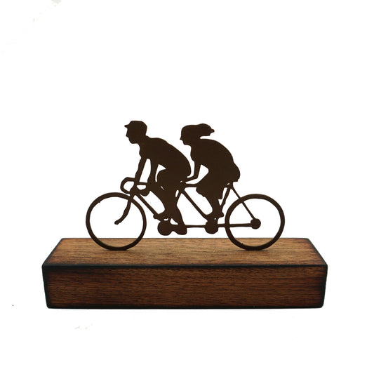 A miniature sculptural artwork by David Mayne featuring a laser cut couple riding a tandem mounted on a hardwood timber block.