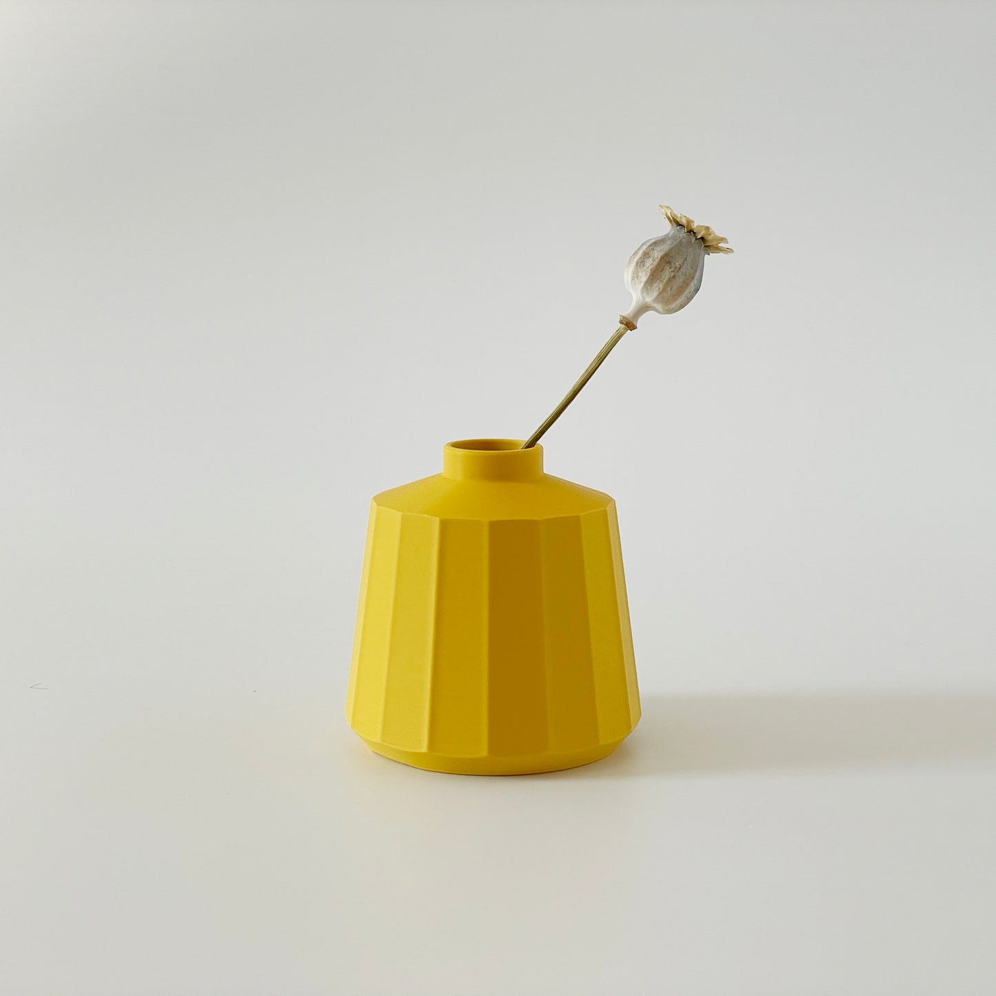 A yellow 3D printed squat vase with a floral decoration inside, set against a white background