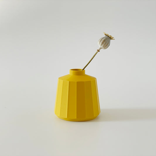 A yellow 3D printed squat vase with a floral decoration inside, set against a white background