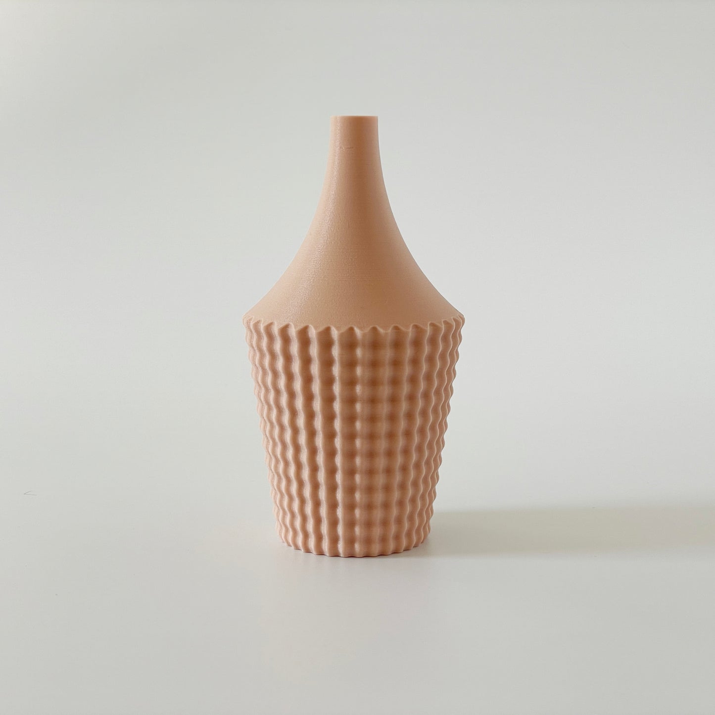 A beige, 3D printed vase with a ribbed design on a white background.
