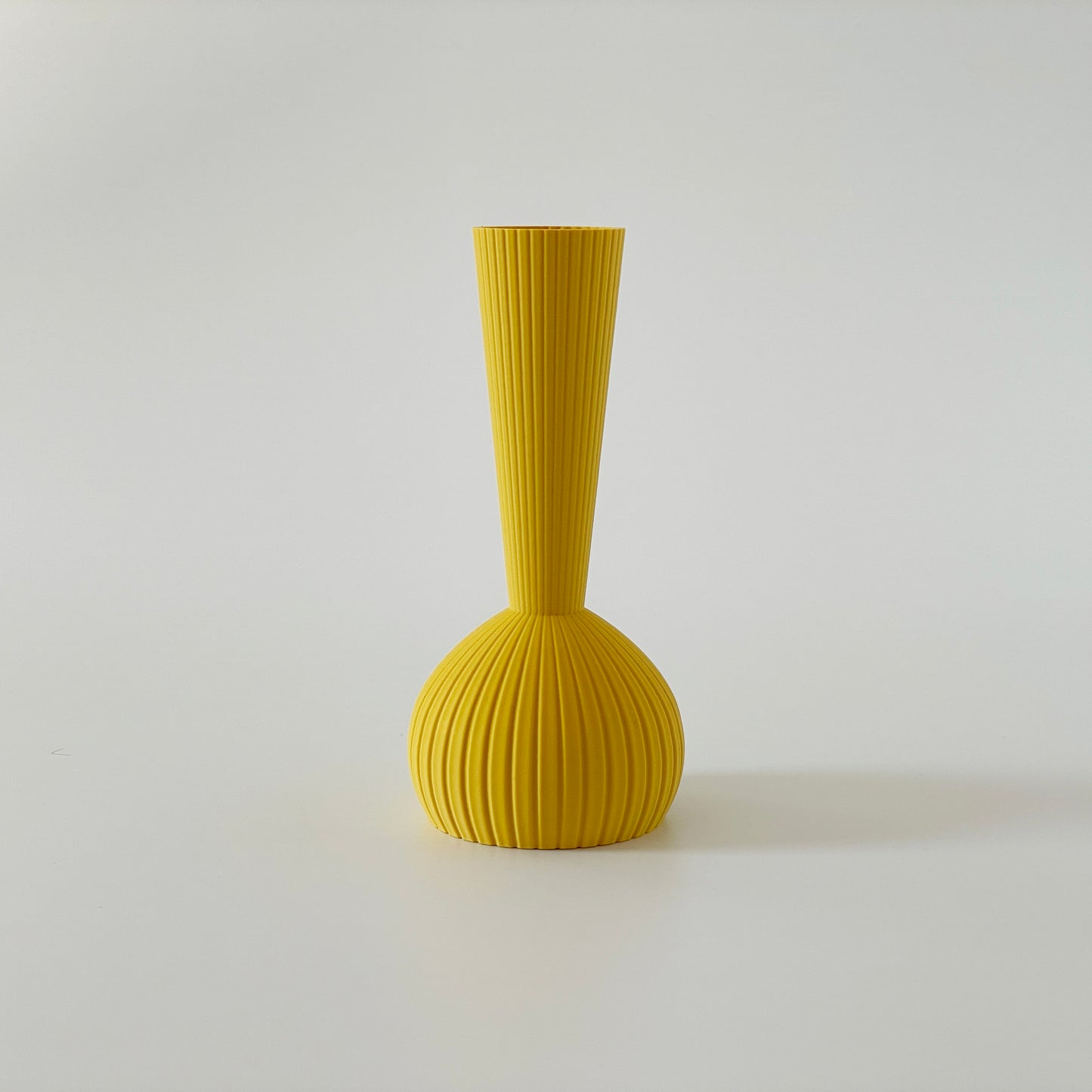 A yellow 3D printed vase with a long bottle neck top, set against a white background