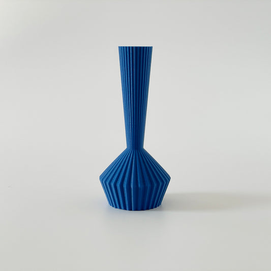 A blue 3D printed vase with a long bottle neck and short bottom with a ribbed texture on a white background.