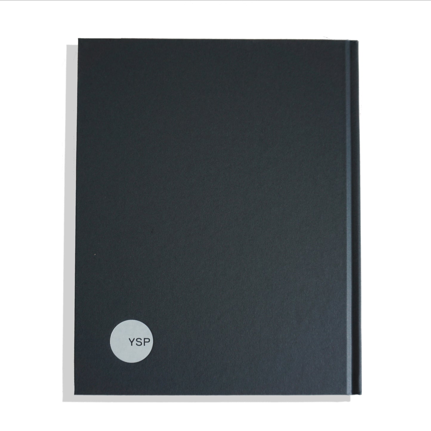 A closed, dark grey notebook with a smooth cover. It features a circular logo in the bottom right corner, displaying the letters "YSP" in a simple font. The notebook is positioned against a plain white background.