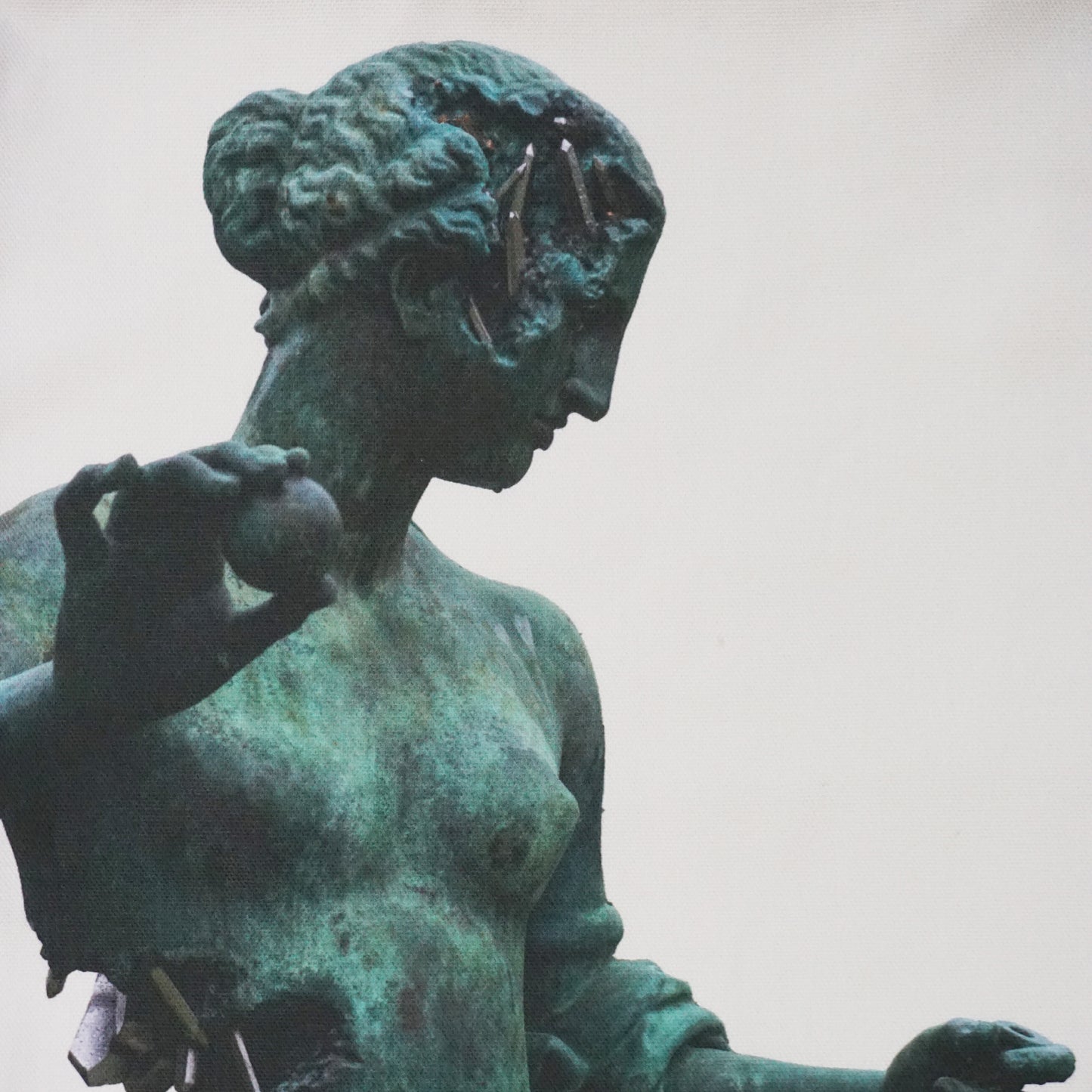 A close-up of a weathered bronze statue of a woman, depicted in profile. She holds a sphere in one hand and gazes thoughtfully. The surface shows signs of age, with patches of green patina and small objects embedded in the figure.