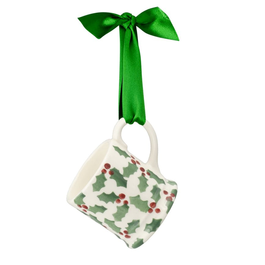 A Christmas hanging ornament shaped like a small white mug decorated with a green holly and red berry pattern, suspended by a bright green satin ribbon bow on a white background.