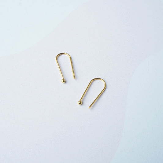 Two gold arch shaped earring on a light grey background