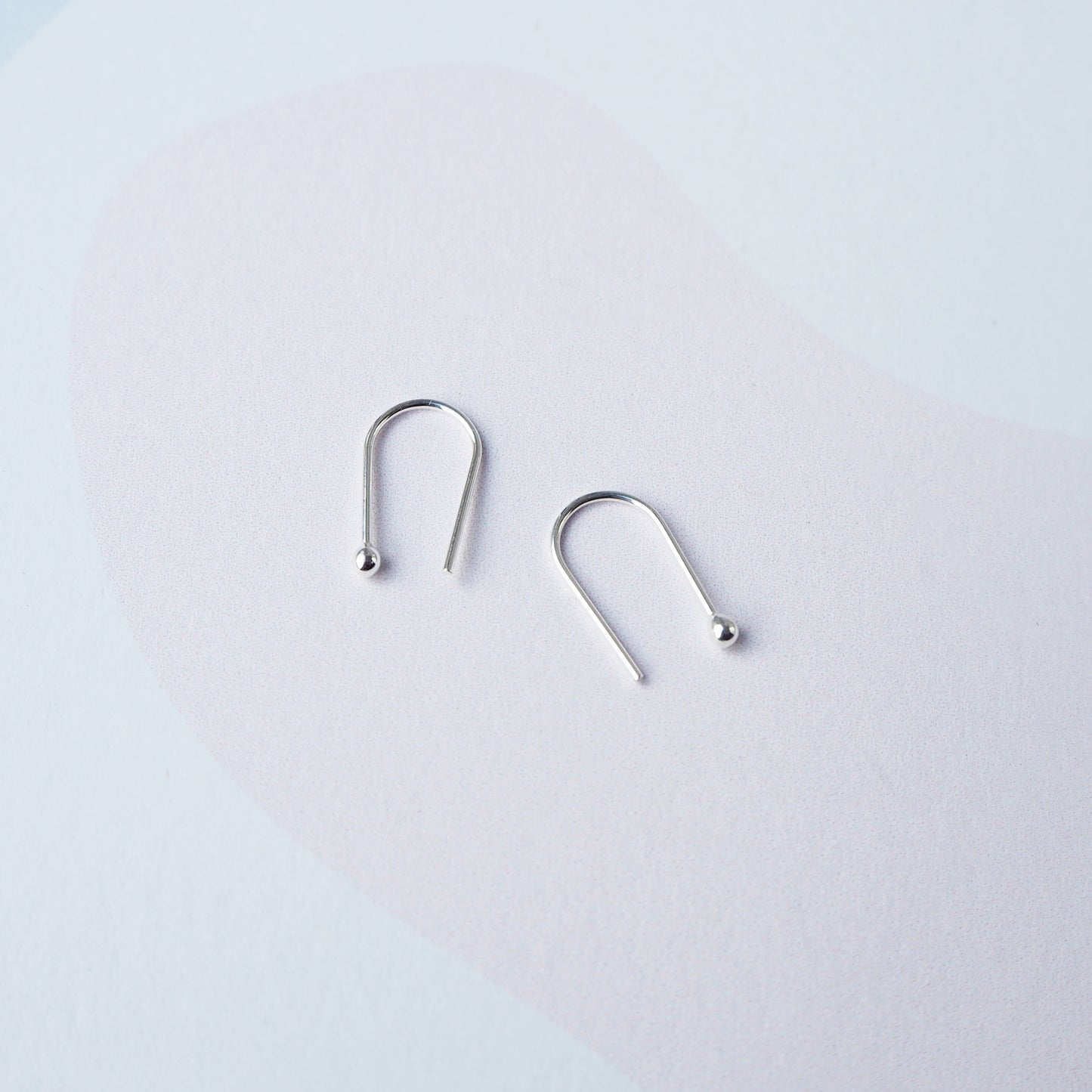 Two silver arch shaped earring on a light grey background