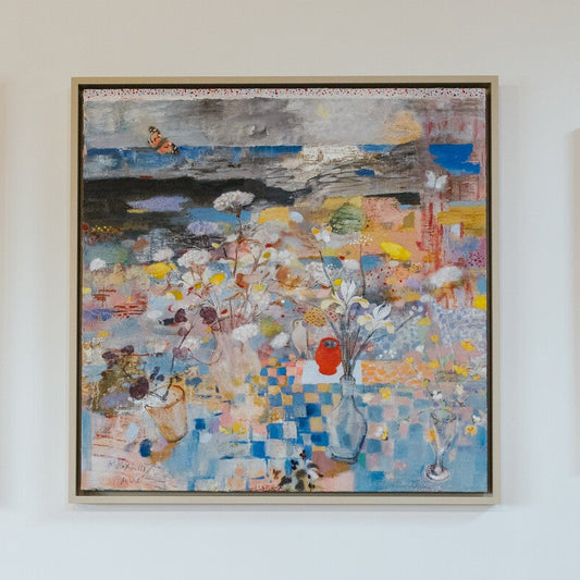 Three colorful abstract paintings on a white wall above tables with chairs.