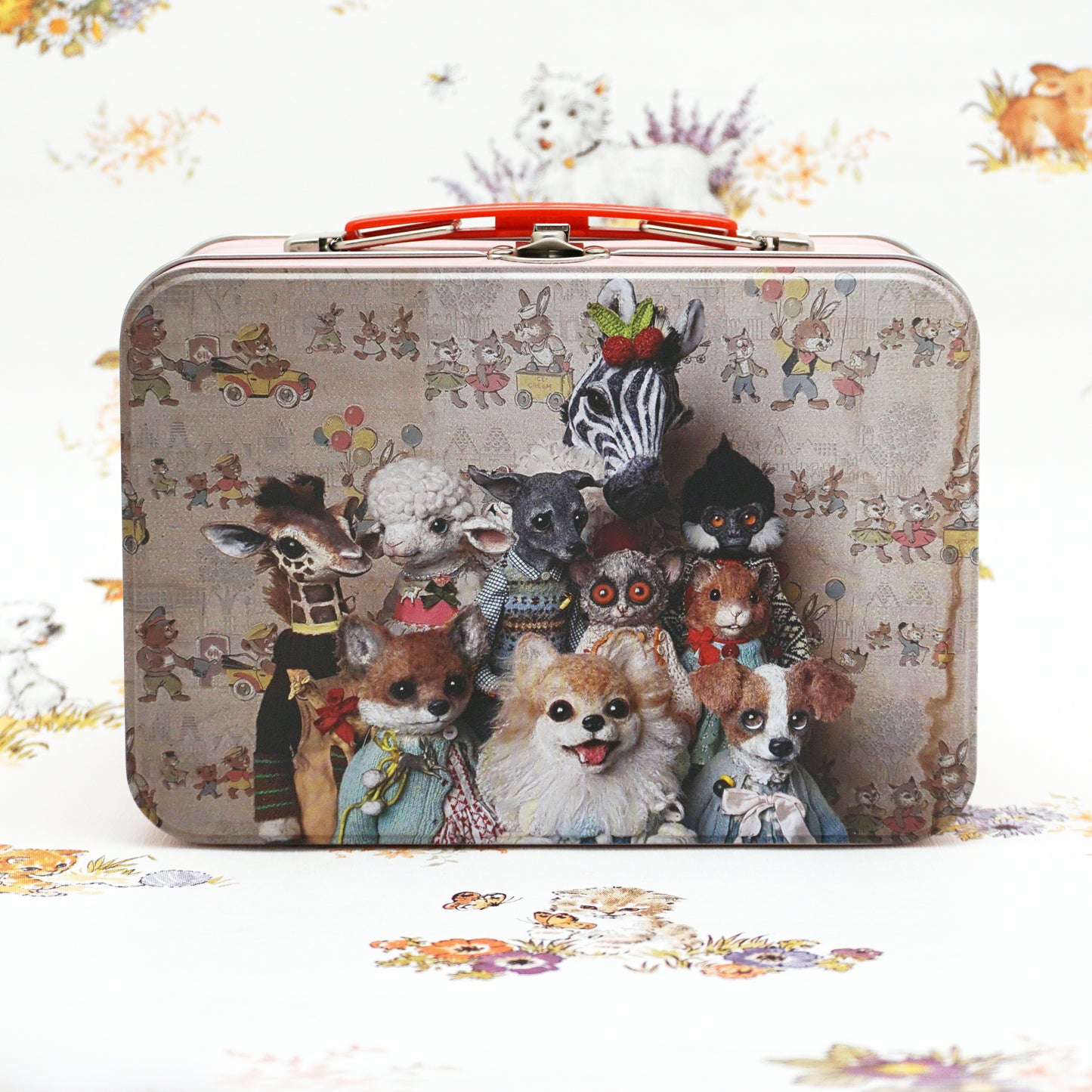 A vintage-style lunch box featuring a whimsical image of various anthropomorphic animals, including a dog, a zebra, and a lamb, all dressed in colourful outfits. The background has a playful floral pattern, enhancing the charming aesthetic.